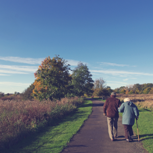 An elderly man and woman walking along a country road.